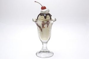 A fountain style glass filled with an ice cream sundae with a straw and a cherry on top.